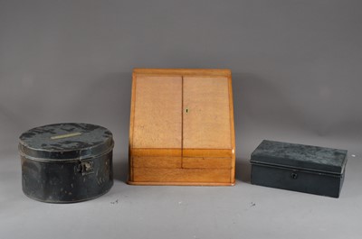 Lot 542 - A 20th century wooden desk tidy (currently locked) 31cm high, a circular metal hat box, with label 'Stevens' to the top, 27cm in diameter and a metal money box (3)