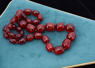 Lot 51 - A string of oval 'cherry amber' knotted strung beads